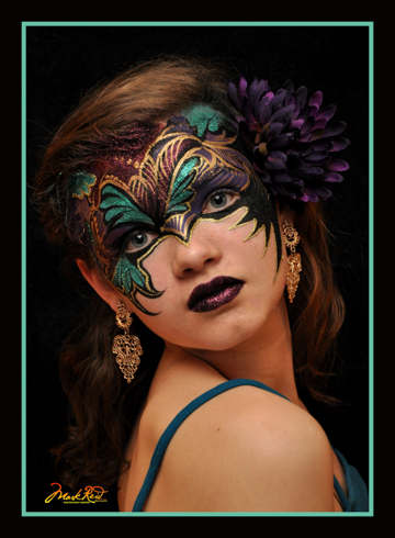 girl with a painted on mask that is mostly black with turqouise and gold notes